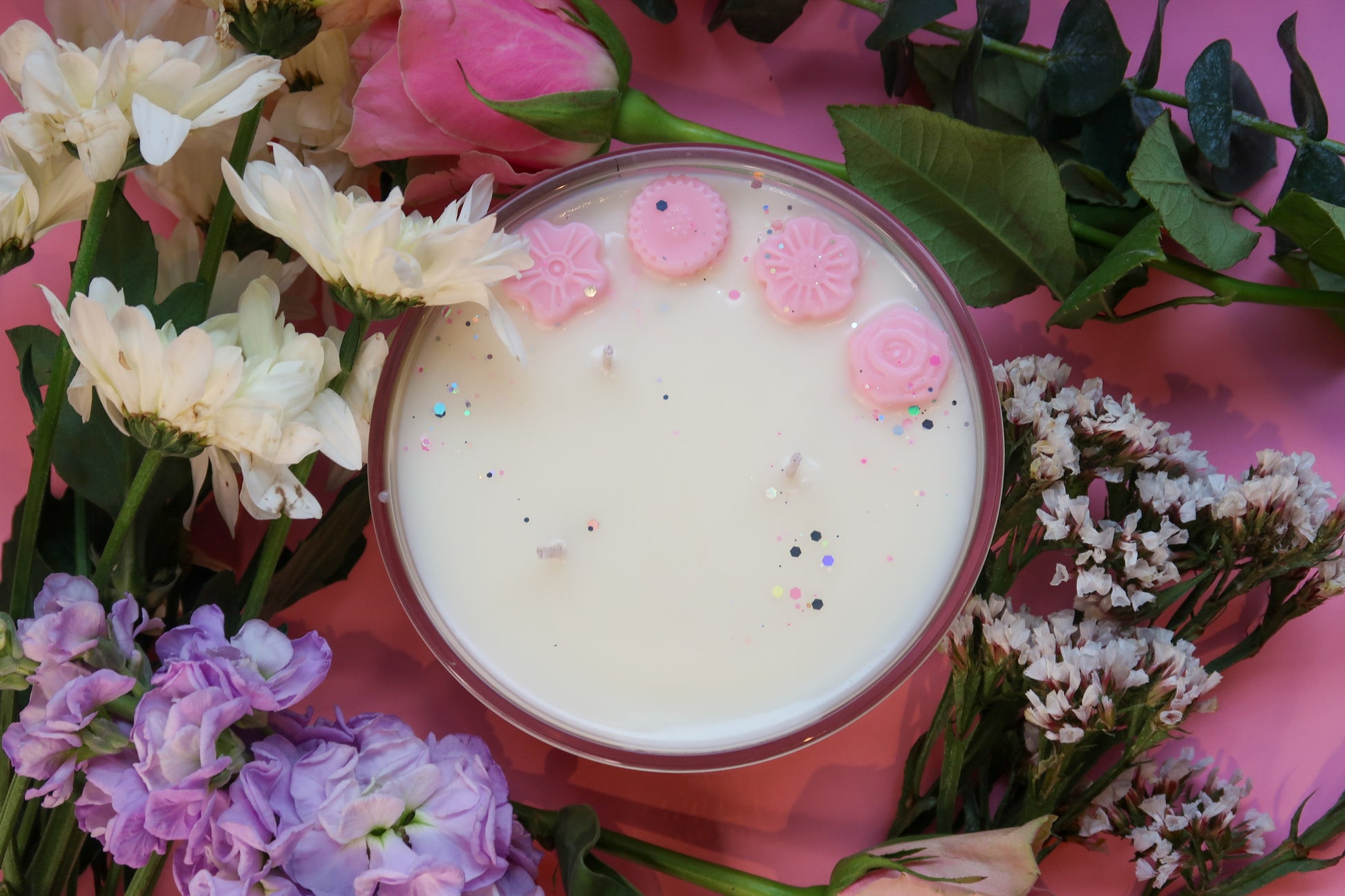 Overhead view of Timeless Aromas Peony Blush Large Candle revealing the three wicks and embellishments, surrounded by an assortment of flowers, ideal for a cozy ambiance.