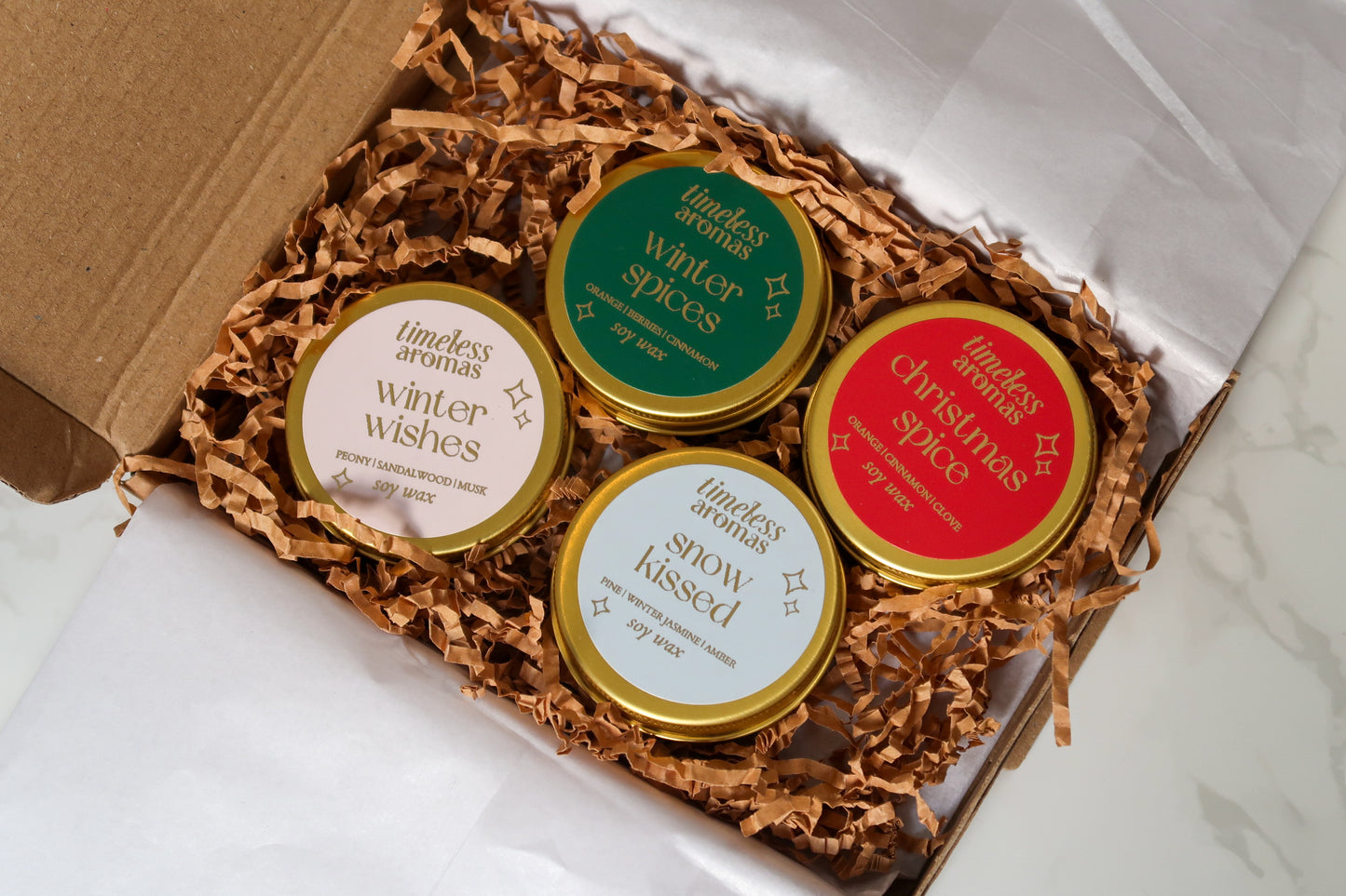 Elegant Mini Christmas Candle Gift Set by Timeless Aromas showcasing four gold tin candles nestled in eco-friendly packaging. Each candle features festive scents perfect for the holiday season.