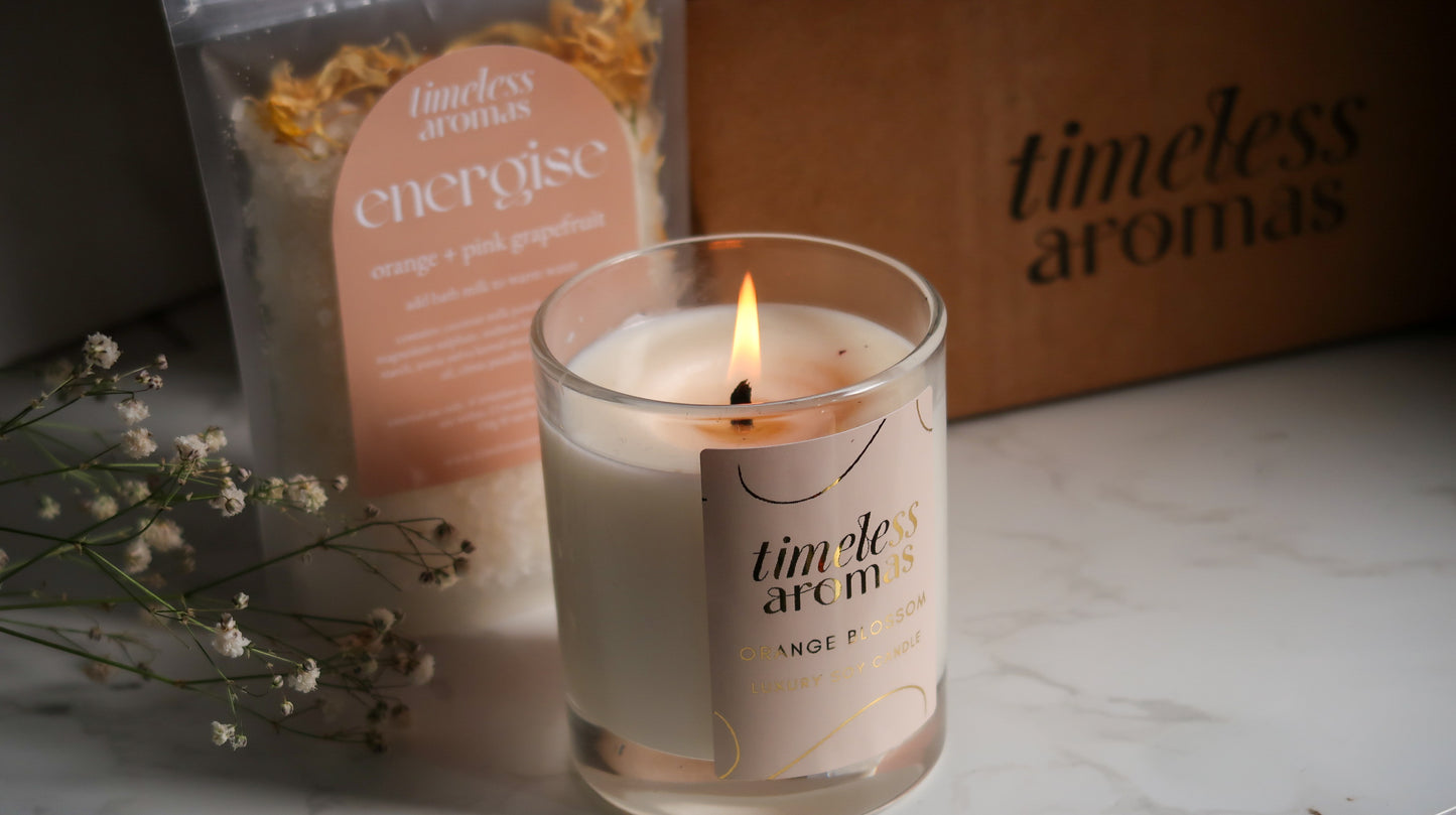 Detailed view of the Timeless Aromas Bloom and Energise Gift Set highlighting the burning orange blossom candle and energise bath milk, a charming home fragrance set filled with 200g of floral orange vibes.