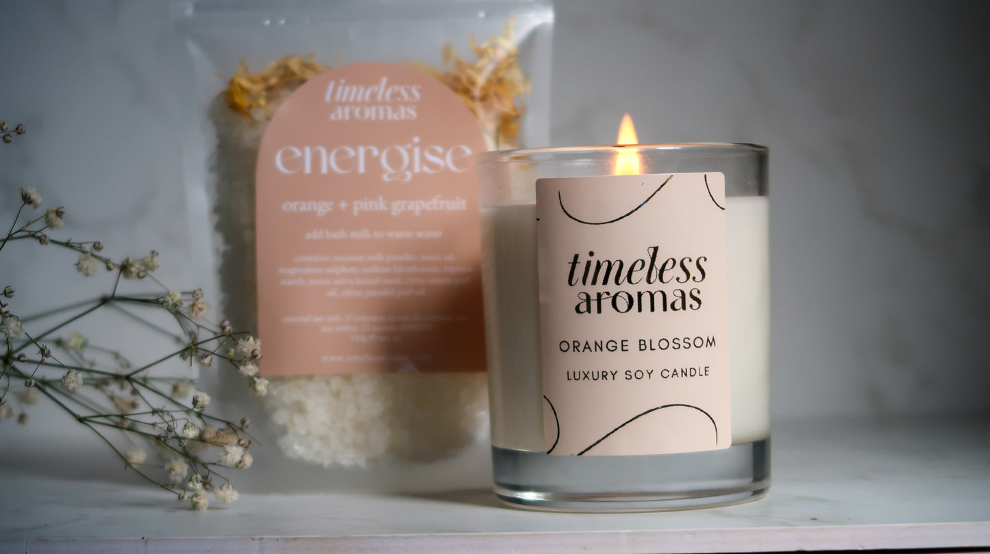 Showcasing the Timeless Aromas Bloom and Energise Gift Set, featuring a 200g orange blossom candle alongside energise bath milk, a perfect combination for a vibrant home fragrance set packed with floral orange vibes.