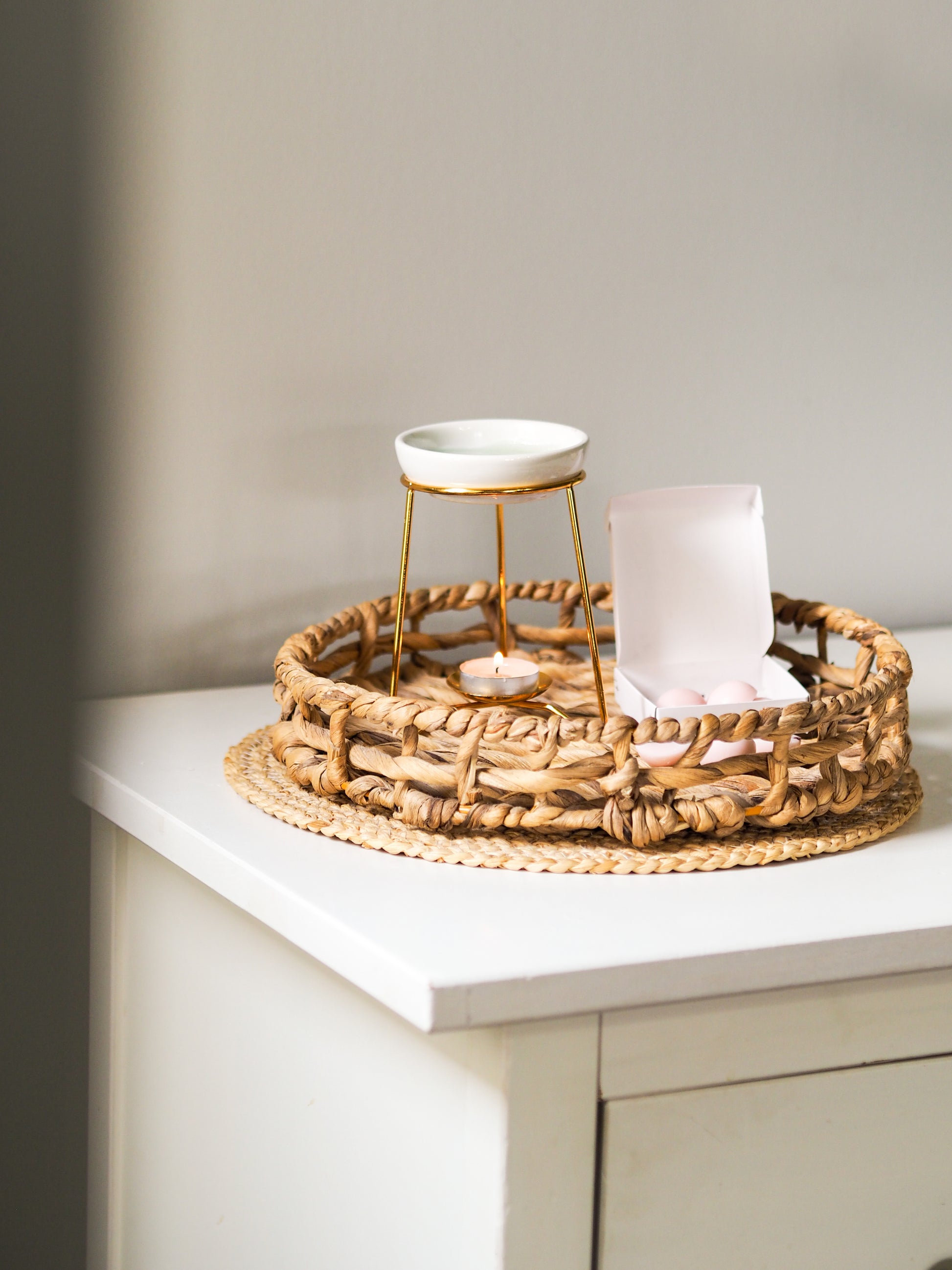 A stylish luxury wax melt burner with a gold frame and white ceramic dish, displayed on a woven tray, by Timeless Aromas. Elevate your scent rituals.