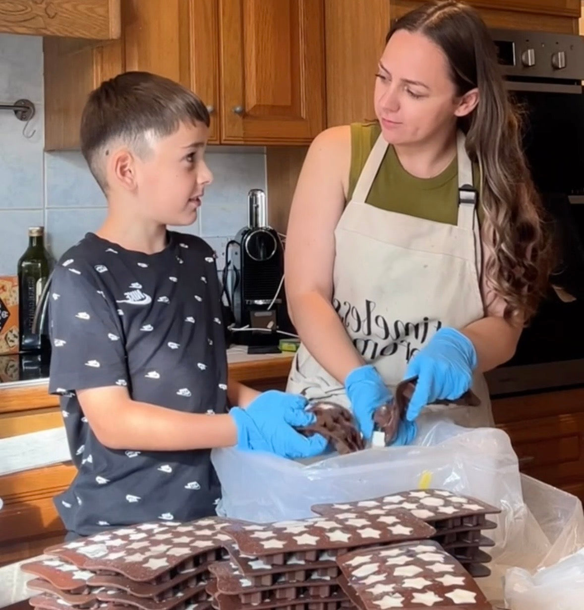 natasha and her son in the kitchen hand pouring and de-moulding wax melts for the timeless self-care club subscription boxes. natasha and her son making handmade wax melts for the timeless aromas self-care subscription boxes. founder natasha and her son creating handmade wax melts for timeless aromas. subscription boxes.